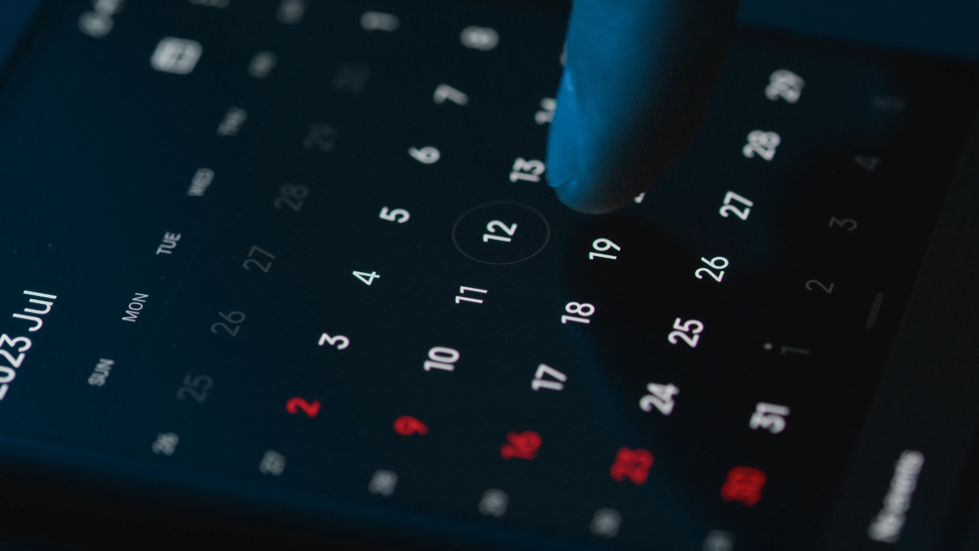 A finger selecting a date on a dark digital calendar